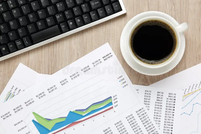 A coffee cup, keyboard, and financial charts on a desk.