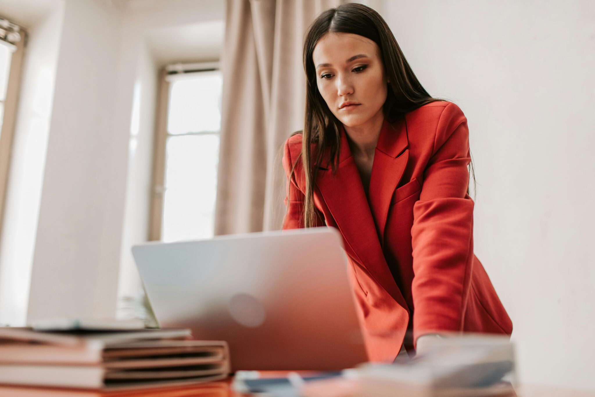 Woman in red blazer focused on laptop reviewing business plans for mid-year check-in
