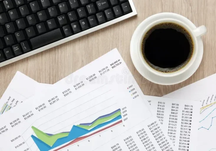 A coffee cup, keyboard, and financial charts on a desk.