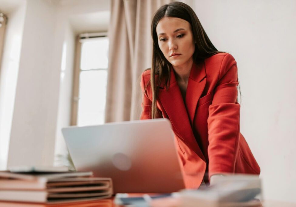 Woman in red blazer focused on laptop reviewing business plans for mid-year check-in