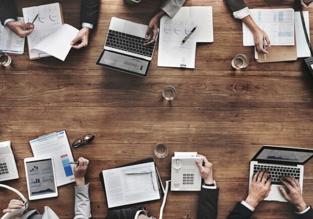 Business meeting with laptops, documents, and calculators on a wooden table.
